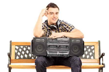 Smiling guy holding a boombox seated on a wooden bench isolated on white backgroundの写真素材