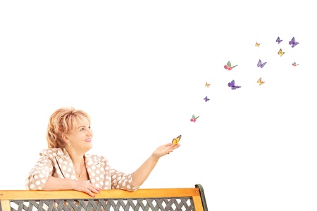 Mature female on a wooden bench and looking at colorful butterflies isolated on white backgroundの写真素材
