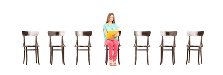 Smiling female student sitting on a wooden chair and writing notes, isolated on white backgroundの写真素材