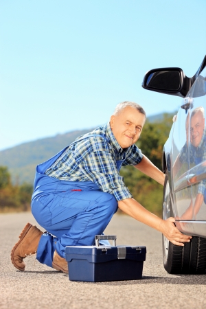 Male mechanic changing a car tyre on an open roadの写真素材