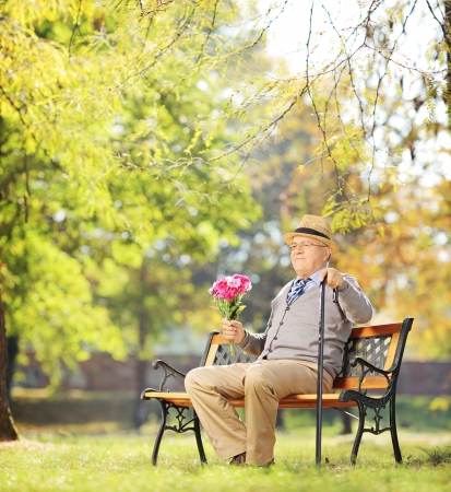 Senior gentleman with bunch of flowers sitting on a wooden bench, in a park, shot with a tilt and shift lensの写真素材