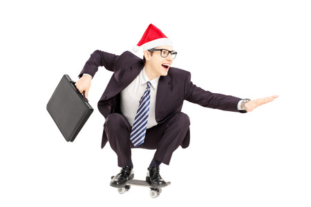 Young smiling businessman with briefcase and santa hat riding a skateboard isolated on a white backgroundの写真素材