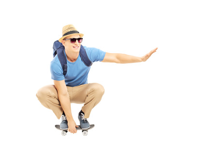 Smiling male student with backpack skating on a skate board isolated on white backgroundの写真素材
