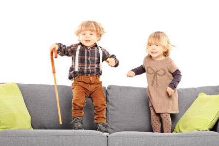 Brother and sister standing and playing on a sofa isolated on white background