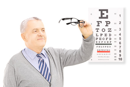 Senior gentleman standing in front of eyesight test holding a pair of glasses, isolated on white backgroundの写真素材