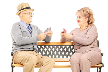 Senior couple playing cards seated on wooden bench isolated on white backgroundの写真素材