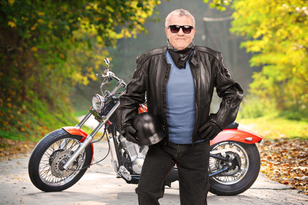 Mature biker in leather jacket standing in front of his chopper on an open road