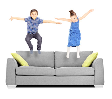 Brother and sister jumping on sofa isolated on white backgroundの写真素材
