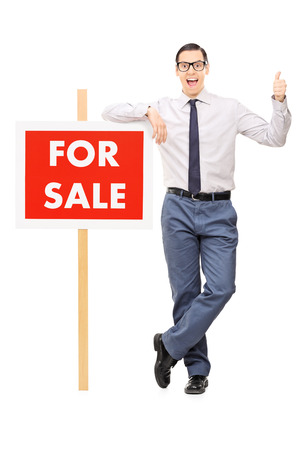 Excited man leaning on a for sale poster and giving thumb up isolated on white backgroundの写真素材