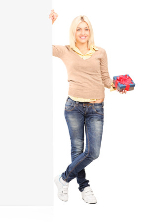 Girl holding a present next to a blank panel isolated on white backgroundの写真素材