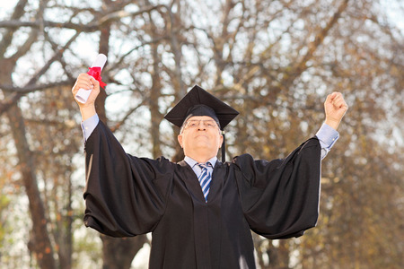 Mature graduate gesturing happiness in parkの写真素材