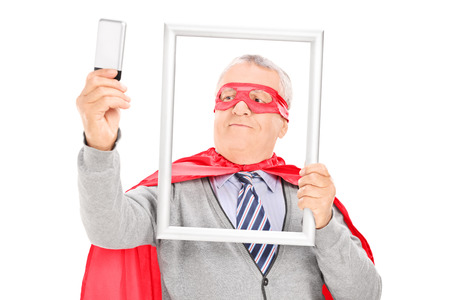 Mature superhero taking a selfie with a picture frame isolated on white backgroundの写真素材