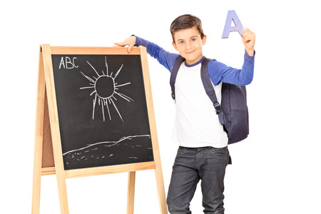 Schoolboy standing by a blackboard and holding the letter a isolated on white backgroundの写真素材