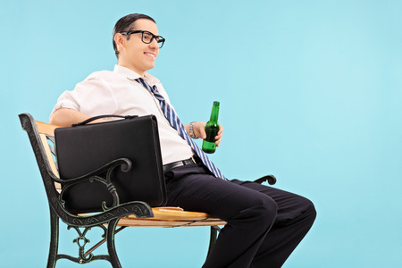 Businessman relaxing with a beer seated on bench against blue background の写真素材