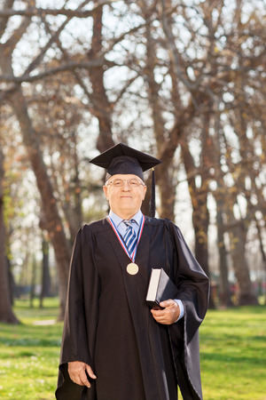 College dean in graduation gown holding a book in a parkの写真素材
