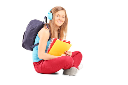 Beautiful female student with backpack sitting on the floor isolated on white backgroundの写真素材