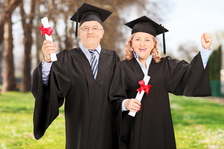 Mature couple celebrating their diplomas and their graduation in parkの写真素材