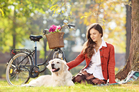 Beautiful female sitting on a grass with her labrador retriever dog in a parkの写真素材