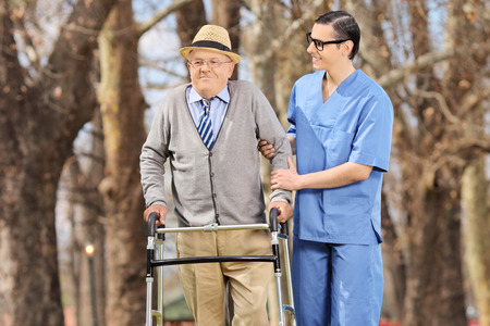 Medical professional helping a senior with walker in a parkの写真素材