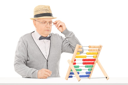 Senior man looking at an abacus seated at table isolated on white backgroundの写真素材