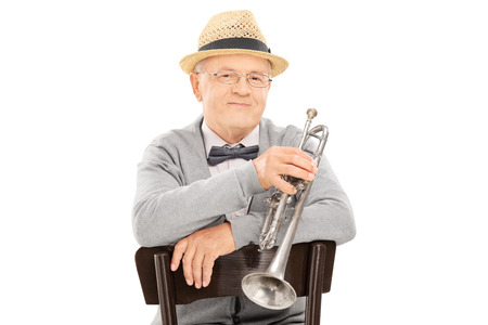Senior gentleman holding trumpet seated on chair isolated on white backgroundの写真素材