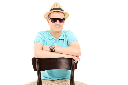 Young man with sunglasses sitting on a chair isolated on white background