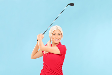 Female golfer swinging a golf club on blue backgroundの写真素材