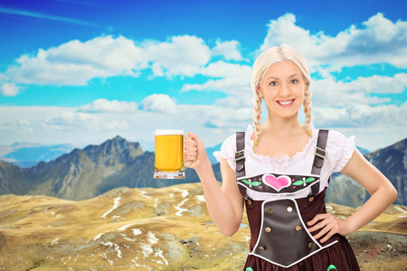 Beautiful Bavarian woman holding a pint of beer somewhere high in the mountainsの写真素材