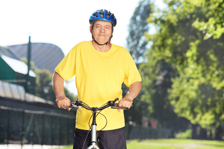 Happy mature male cyclist posing in a park with bike の写真素材