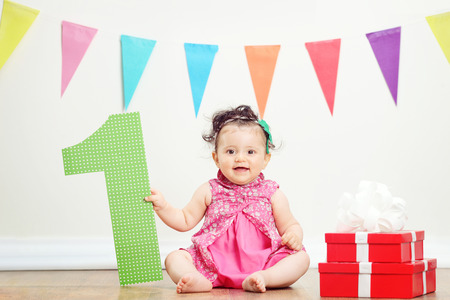 Baby girl sitting by a bunch of presents on a birthday partyの写真素材