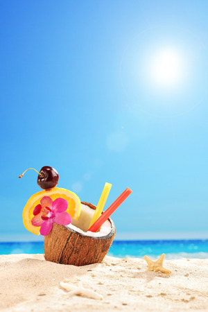 Vertical shot of an exotic cocktail in a coconut on a tropical beach on a sunny summer day の写真素材