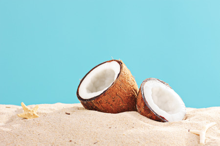 Studio shot of a sliced coconut on a sandy surface on blue backgroundの写真素材