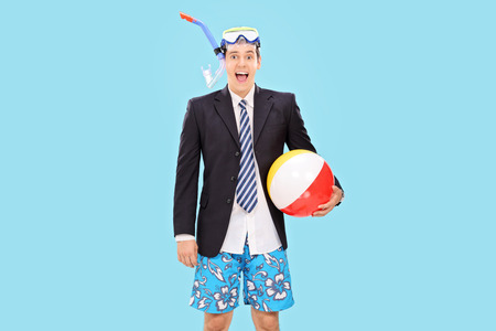Excited businessman with a snorkel holding a beach ball on blue の写真素材
