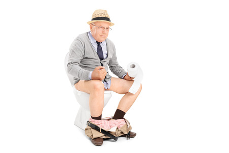 Senior man pushing hard seated on a toilet isolated on white backgroundの写真素材