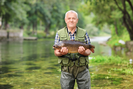Mature fisherman standing in river and holding a fish outdoorsの写真素材