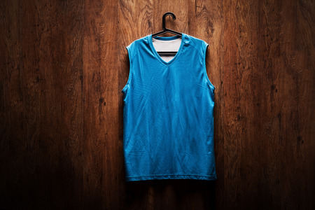 Blue basketball jersey hanging on a wooden wall on a hangerの写真素材