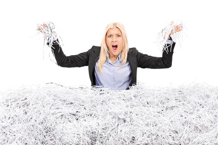 Angry businesswoman in a pile of shredded paper isolated on white backgroundの写真素材