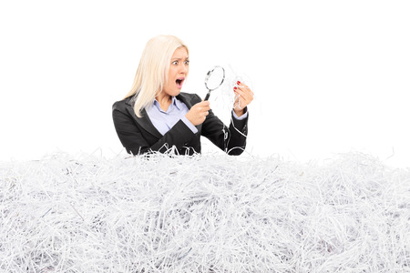 Shocked woman looking at a pile of shredded paper through a magnifier isolated on white backgroundの写真素材
