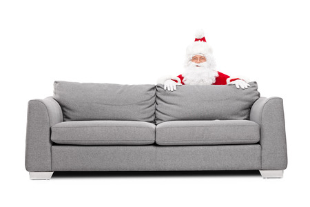 Santa Claus hiding behind a sofa isolated on white backgroundの写真素材