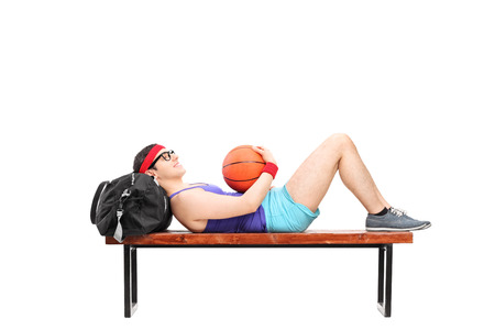 Young man lying on a bench and holding basketball isolated on white backgroundの写真素材