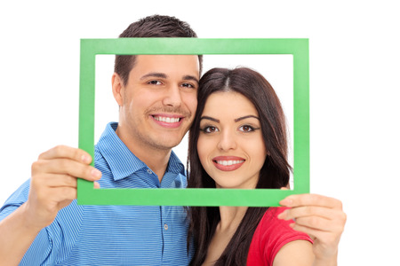 Couple posing behind a green picture frame isolated on white backgroundの写真素材