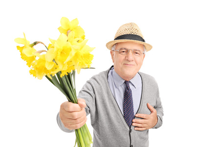 Kind senior gentleman giving flowers to someone and looking at the camera isolated on white backgroundの写真素材