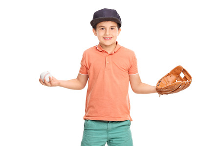 Little boy in an orange shirt and blue cap, wearing a baseball glove and holding a baseball isolated on white backgroundの写真素材