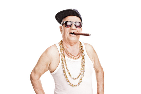Toothless senior with a hip-hop cap and a gold chain around his neck smoking a cigar isolated on white backgroundの写真素材