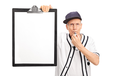 Elderly baseball coach holding a clipboard with a blank paper on it and blowing a whistle isolated on white backgroundの写真素材