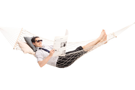 Relaxed young man reading a newspaper and lying in a comfortable hammock isolated on white backgroundの写真素材