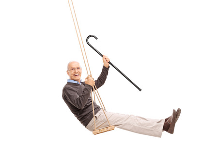 Studio shot of a joyful senior swinging on a swing and holding a cane isolated on white backgroundの写真素材