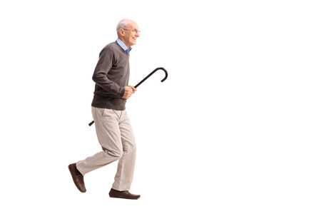 Full length portrait of a joyful senior gentleman carrying a cane in his hand and running isolated on white backgroundの写真素材