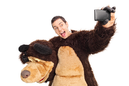 Studio shot of a man in a bear costume taking a selfie with his cell phone isolated on white...