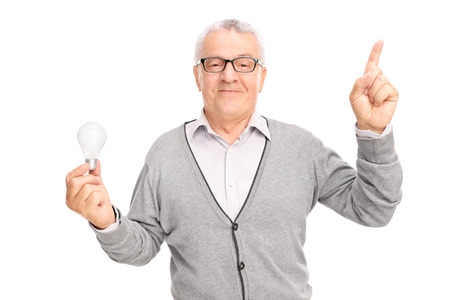 Senior gentleman holding a light bulb and pointing upwards with his finger isolated on white backgroundの写真素材